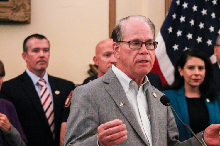 Mike Braun is a White man, balding with dark gray hair. He is wearing glasses and a gray sport coat over a white shirt. Aaron Freeman is a White man with dark hair. He is wearing a black suit with a blue shirt and a white and red striped tie.