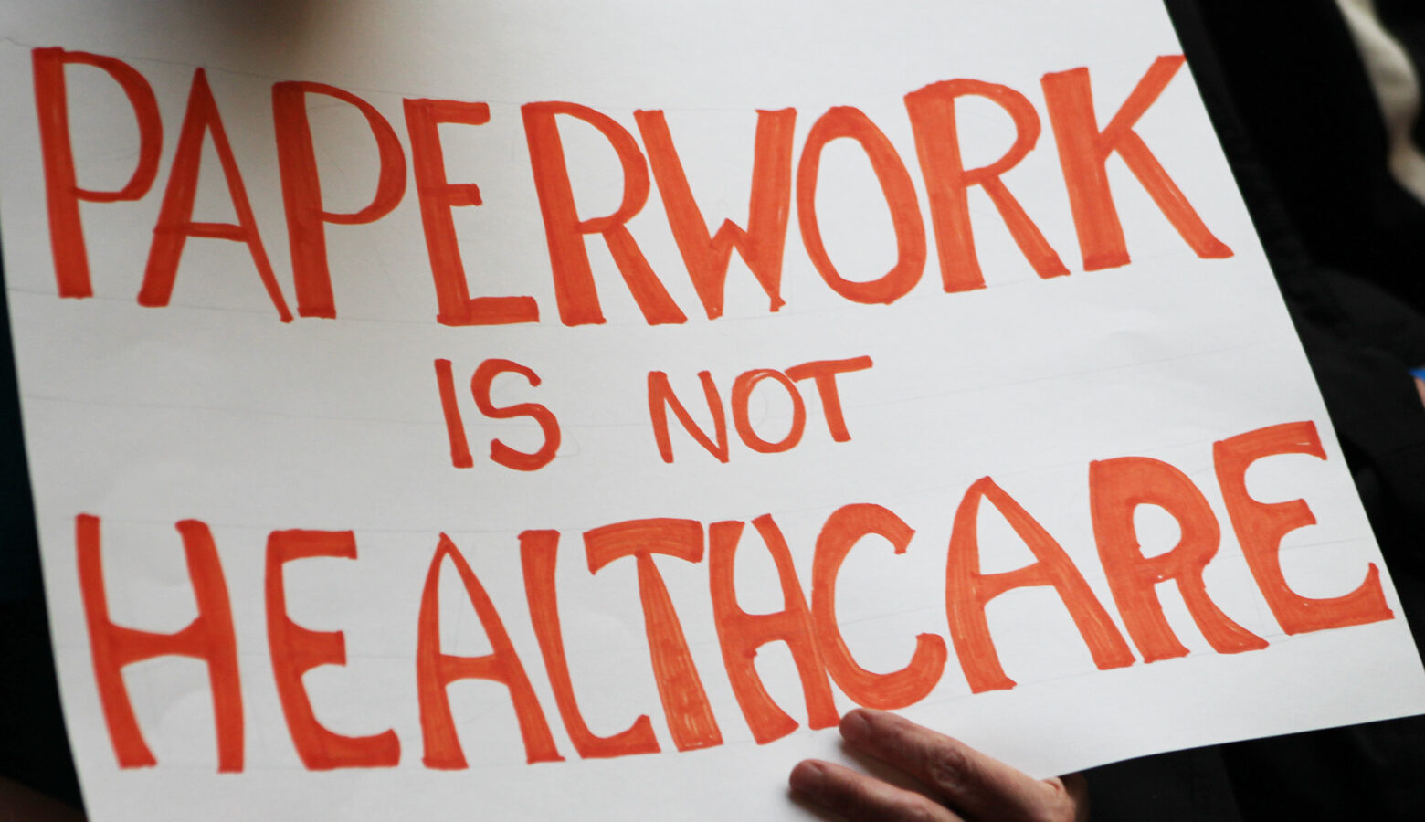 A sign that reads "Paperwork is not healthcare" in bright orange text.