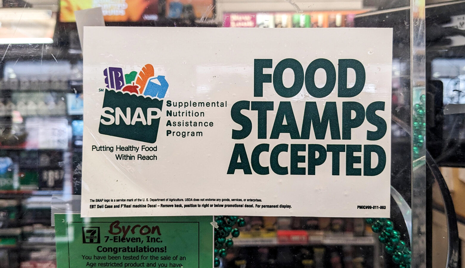 A sign at a grocery store has the SNAP logo on one side, while the other side reads "Food Stamps Accepted."