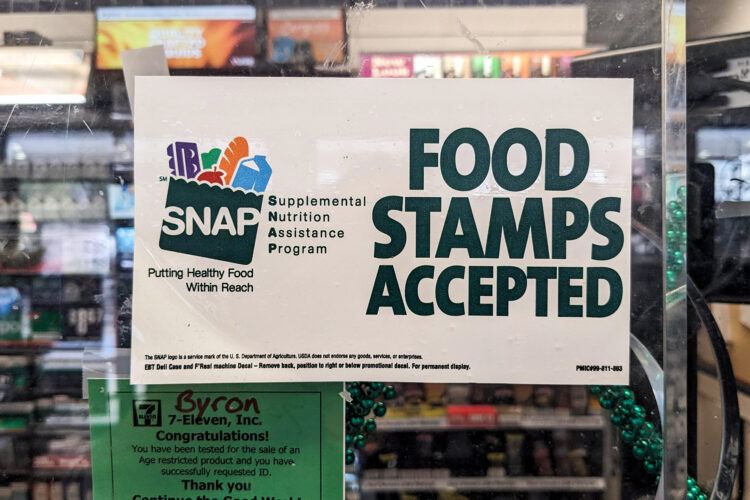 A sign at a grocery store has the SNAP logo on one side, while the other side reads "Food Stamps Accepted."