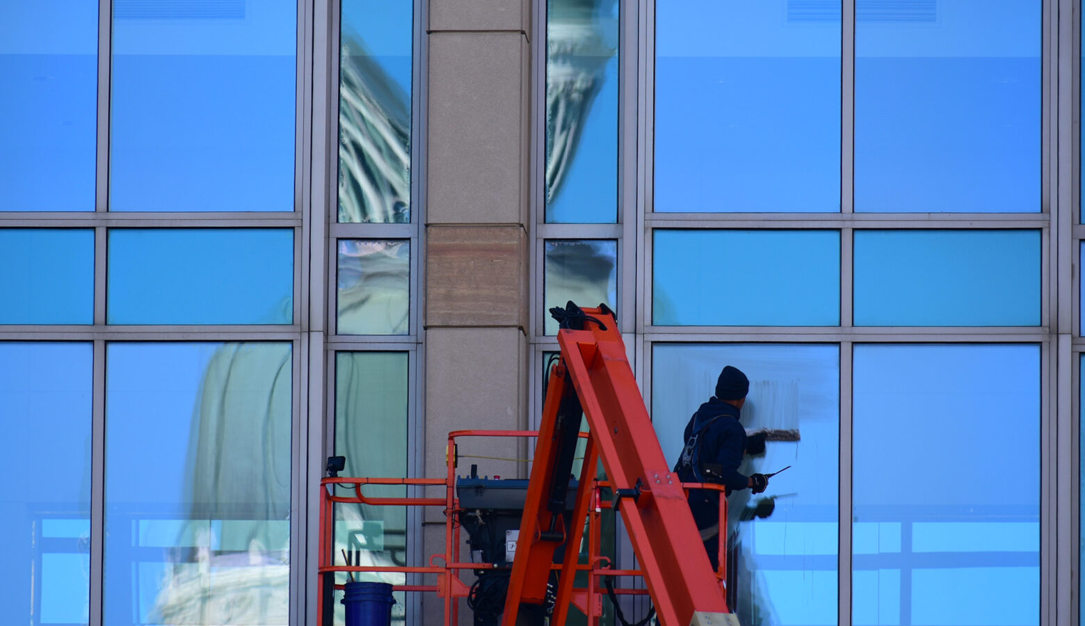A window washer works on a building across the street from the Indiana Statehouse. You can see the Statehouse reflected on the windows.