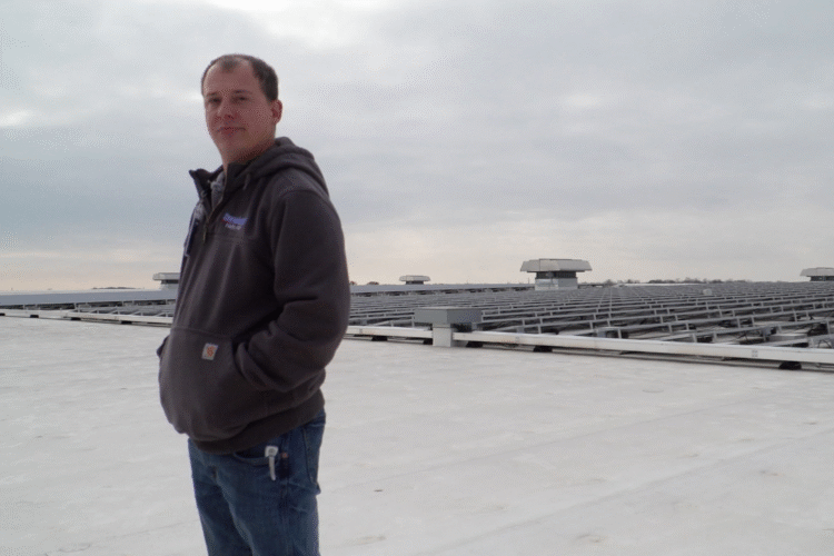 Tyler Gerardot stands in front of the solar array he helps maintain on top of Sweetwater Sound's distribution center in Fort Wayne.