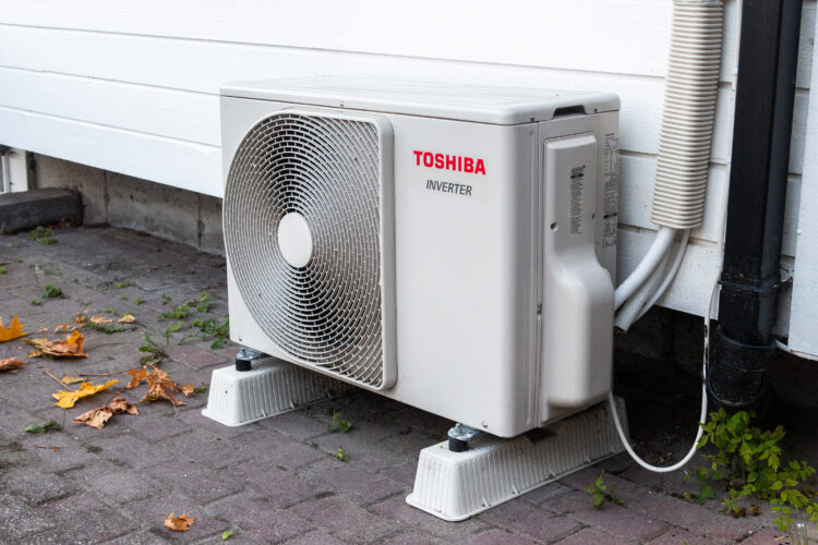 A Toshiba inverter heat pump sits outside of a building. It's a rectangular box with a fan on its outside.