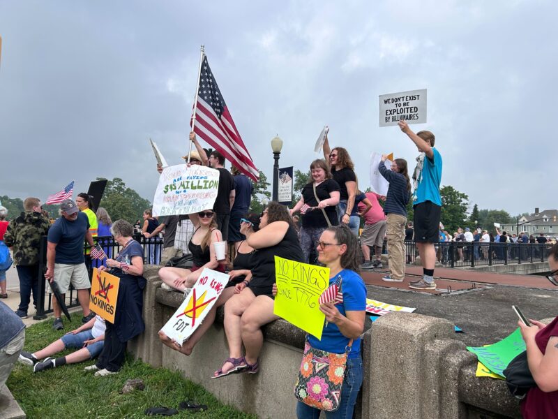 Multiple people sit on a stone fence holding protest signs.