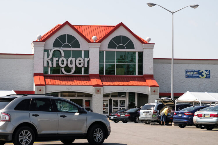 The exterior of a Kroger in Richmond. The brand's logo is displayed outside of large windows. In the foreground are rows of cars in its parking lot.