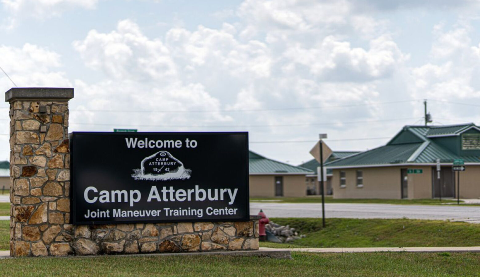 A front gate view of the Camp Atterbury sign with buildings in the background.