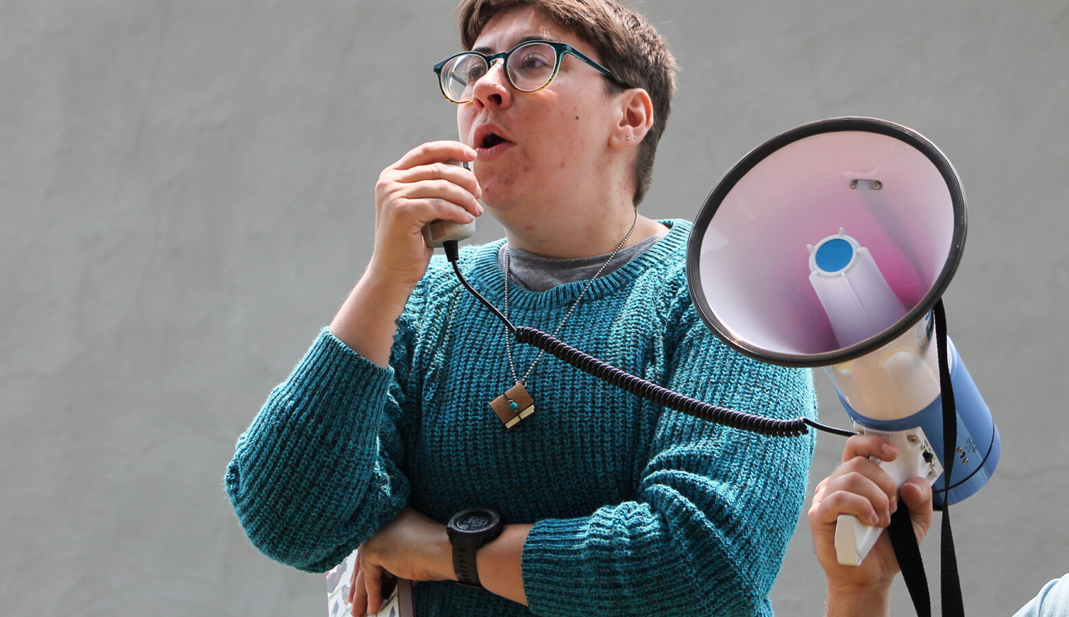 Evie Phelps speaks into a transmitter for megaphone. The megaphone held by another person off-camera.