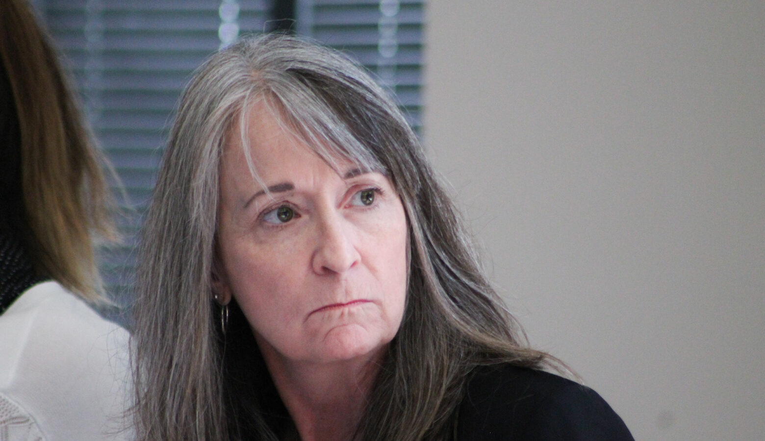 Holly Wimsatt, director of the Bureau of Disabilities Services within FSSA, listens to advocate questions at a Division of Disability and Rehabilitative Service Advisory Council meeting. She is a white woman with bangs and long hair that is mostly grey, but brown in some sections. She wears a black blazer.