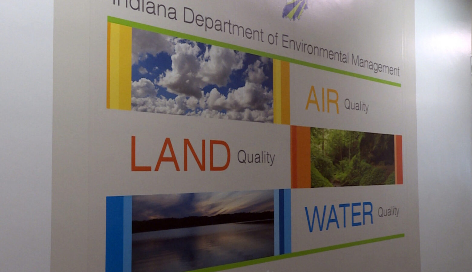 A sign at the entrance to the Indiana Department of Environmental Management's offices in Indianapolis. It reads, "Air quality, land quality, water quality" with photos of the sky, a forest and a lake, respectively.