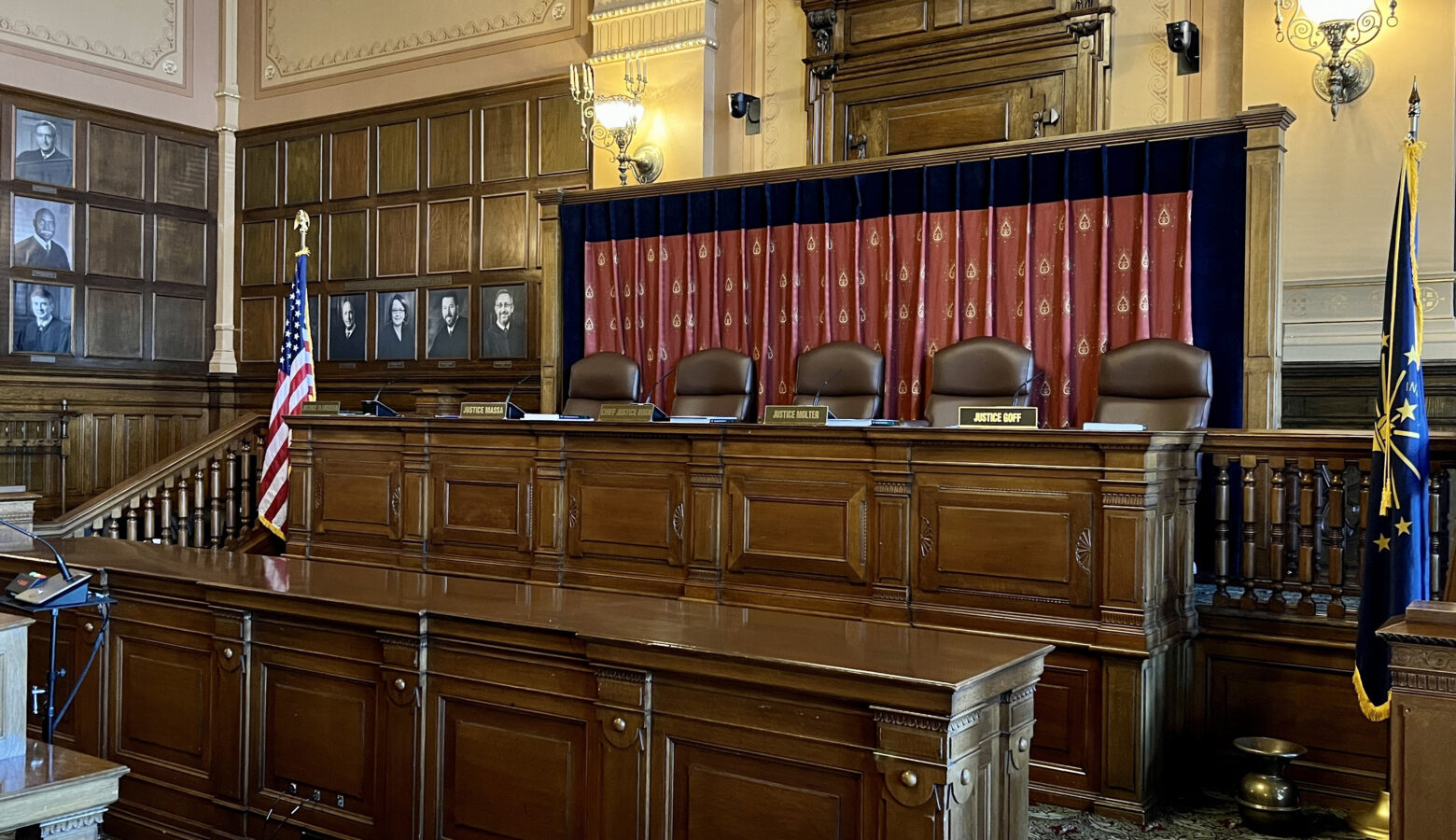 There are five seats at a long, elevated desk. In front of each seat is a name plate with the names of Supreme Court justices.