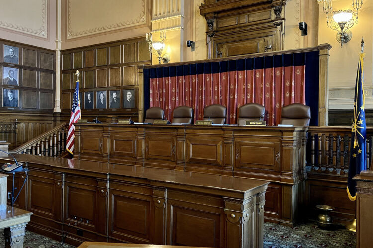 There are five seats at a long, elevated desk. In front of each seat is a name plate with the names of Supreme Court justices.
