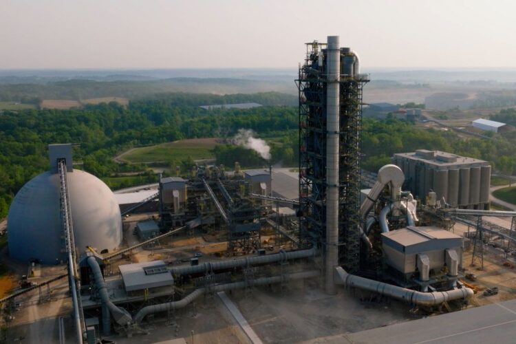 An exterior wide shot of the Heidelberg cement plant in Mitchell. In the photo are a dome on the left of frame, numerous large pipes, a tall and wide pipe bedecked tower, and a block of silos on frame right.