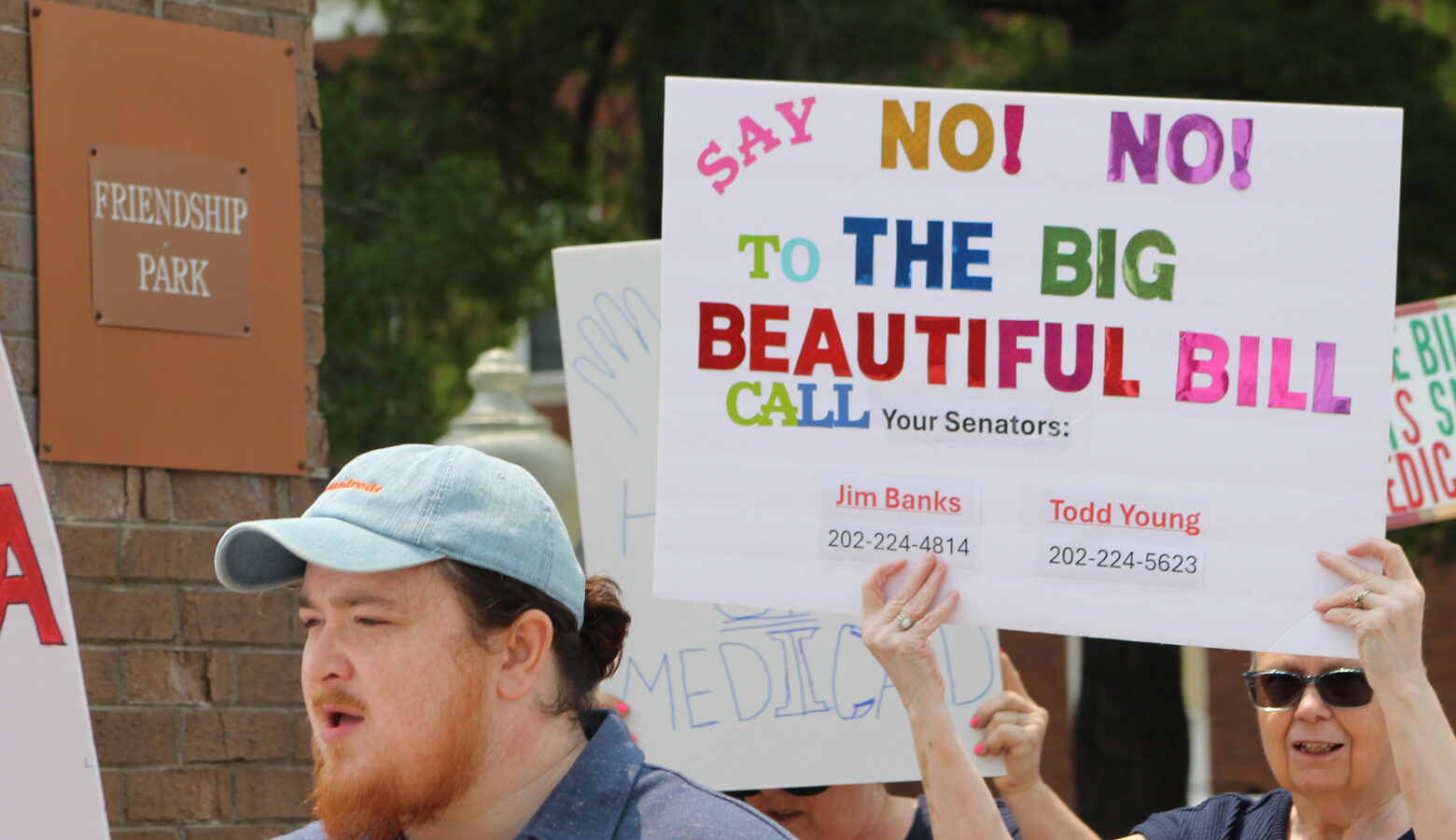 People marching and holding signs, one sign reads "Say No! No! To the Big Beautiful Bill. Call your Senators: Jim Banks 202-222-4814, Todd Young 202-224-5623."