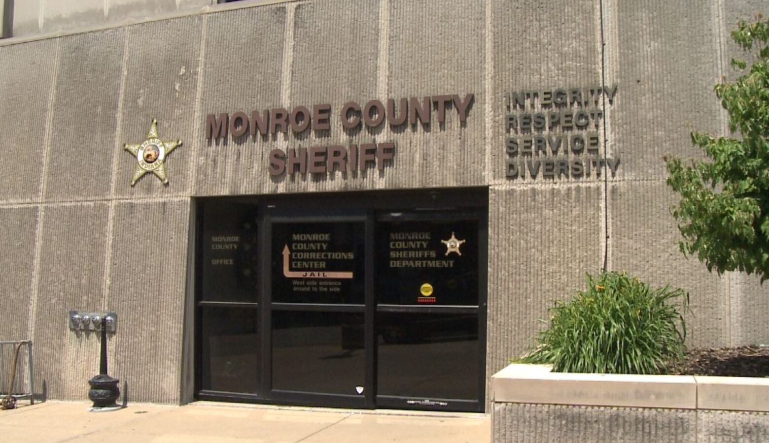 Exterior front door of the Monroe County Sheriff's Department Building in Bloomington. The structure appears to be of stone and concrete with dark-glass sliding doors.