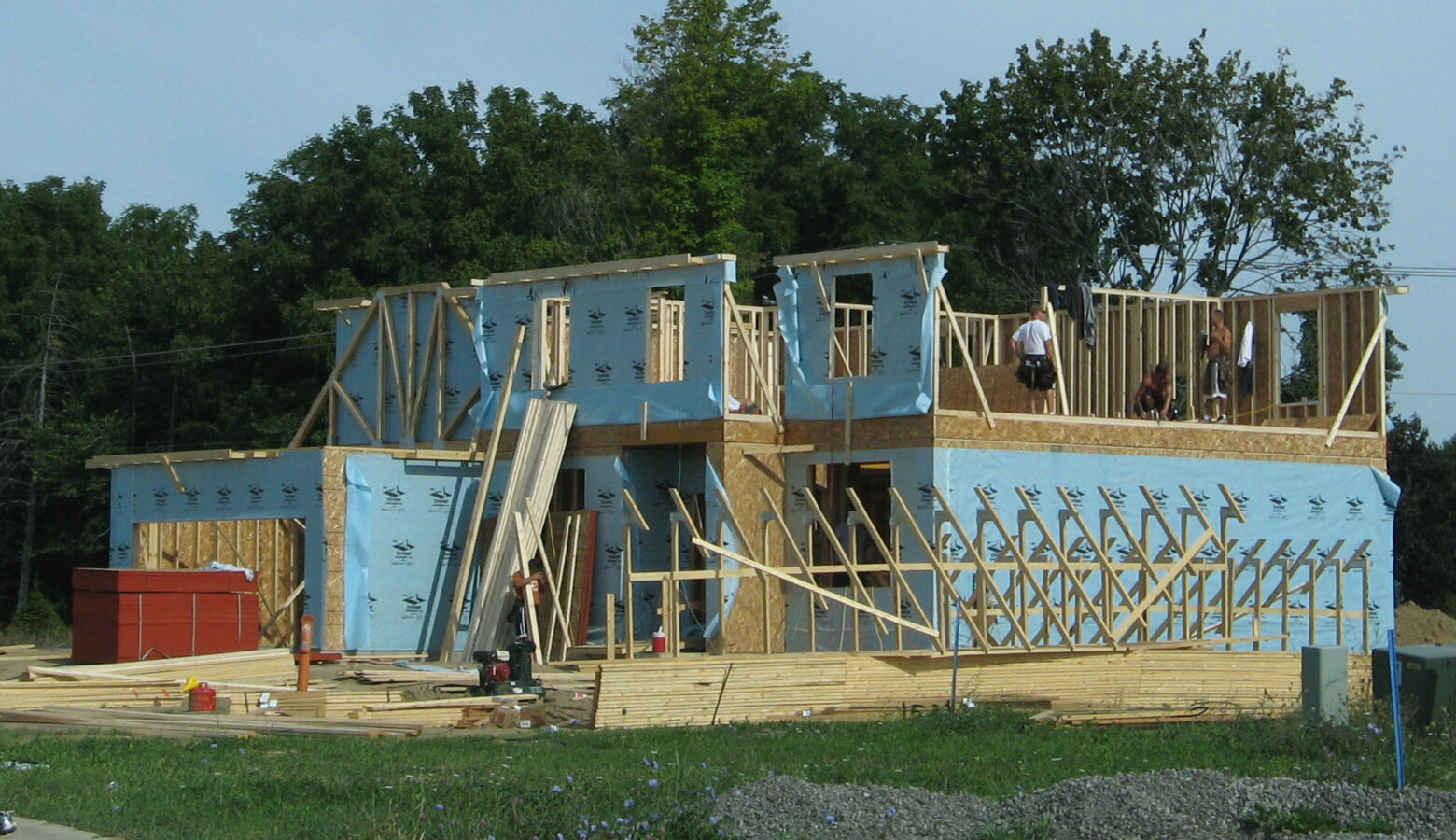 A new home under construction. It's a two story building. Some of the exterior walls are covered with blue sheets, with the rest of it exposed wood beams and walls.