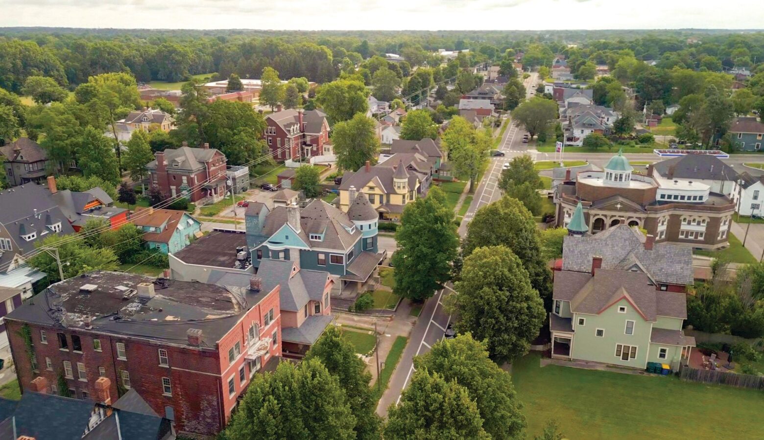 A neighborhood of large historical homes is seen from above, with many trees and a road running through the center.