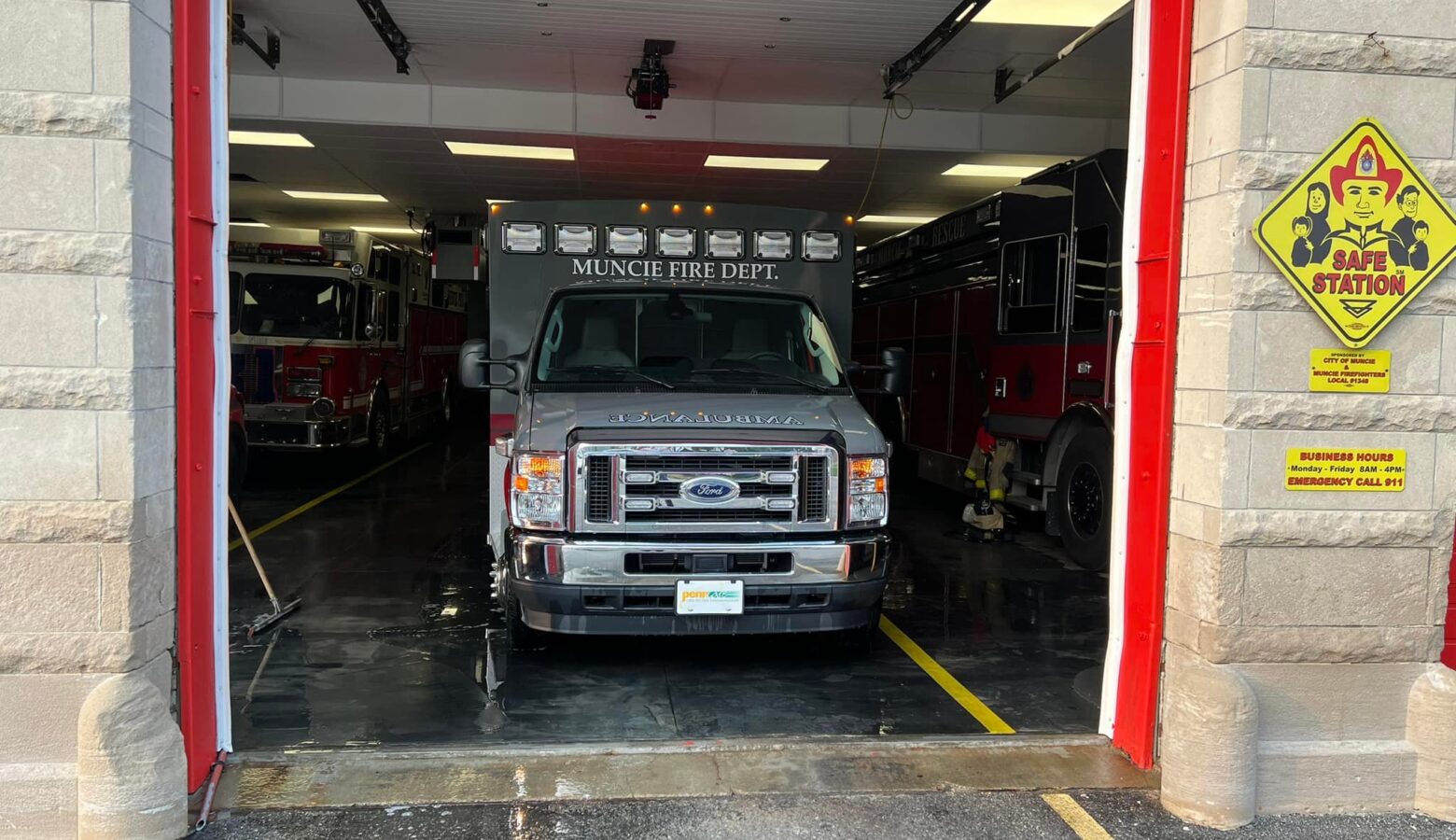 A gray hooded ambulance sits inside a bay at a Muncie fire department station with the garage bay door open.