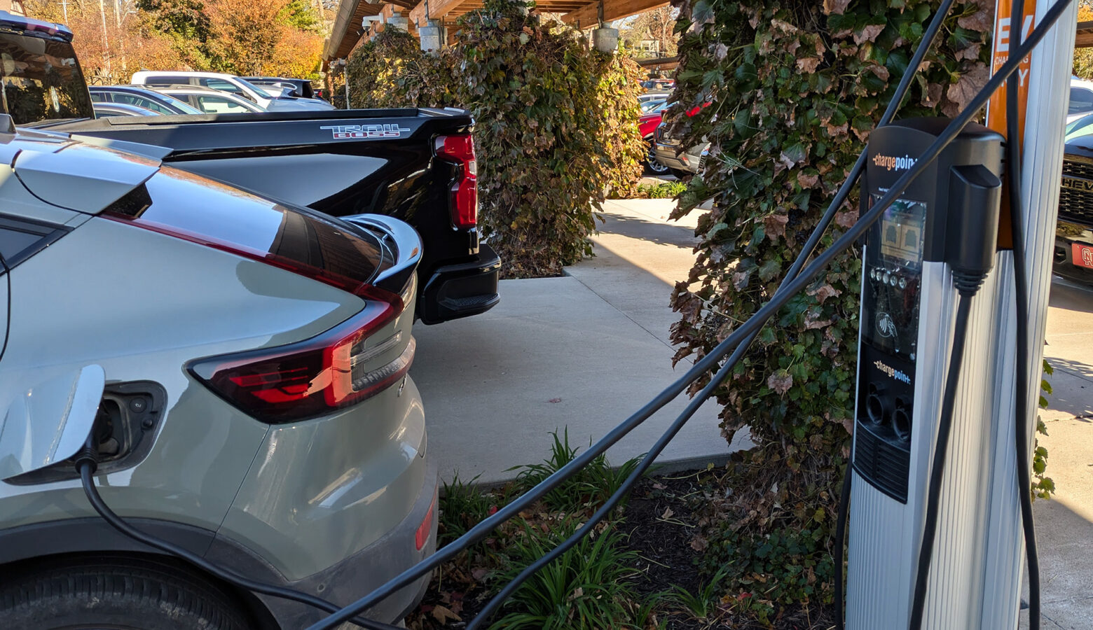 A closeup of a silver sedan with a charging cord running to a small, individual charging port.