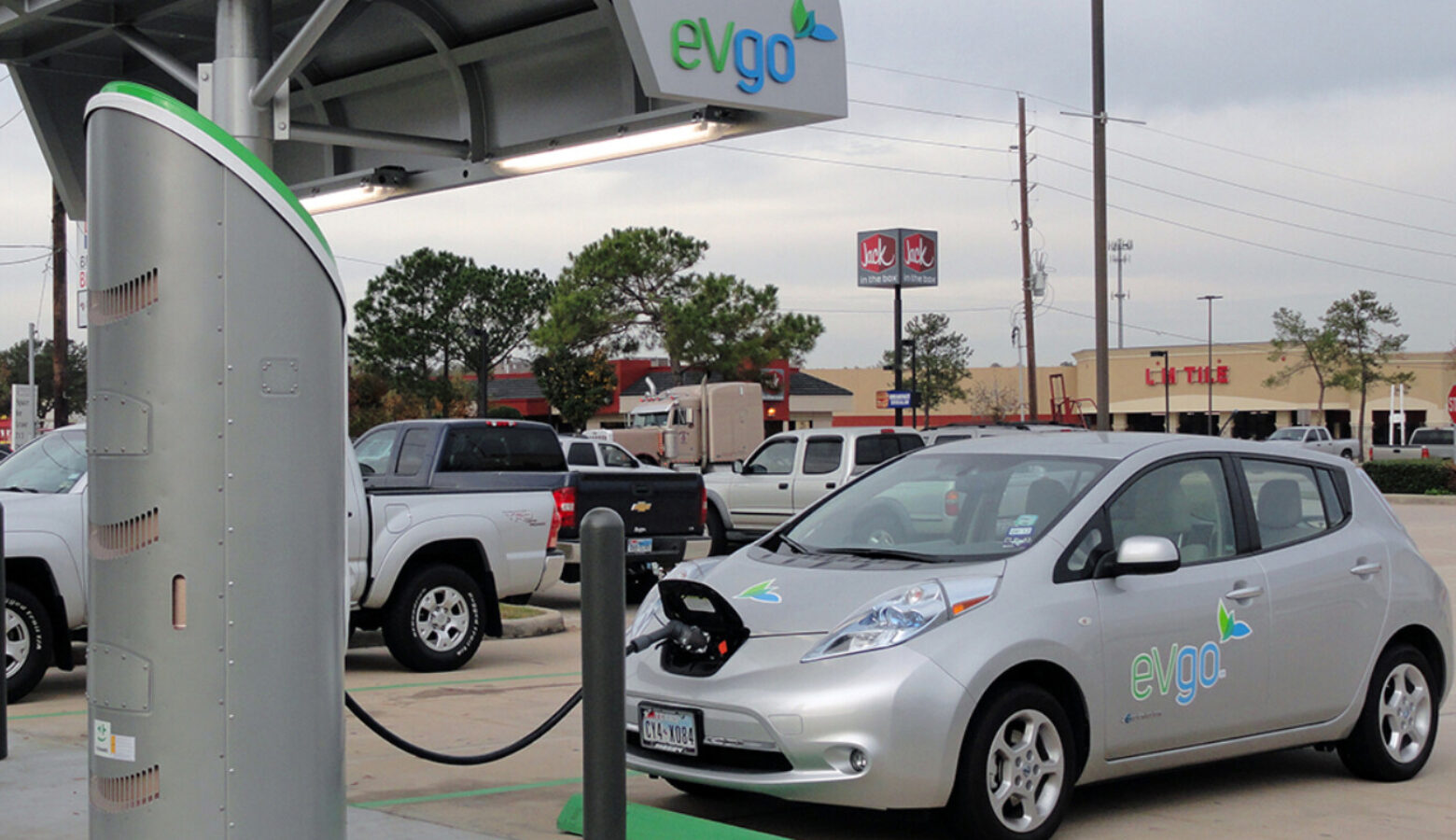 An EV charging pump that looks like a traditional gas pump is plugged into a the silver car. A sign above the car reads eVgo.