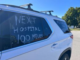 The side of a white car with the words "Next Hospital 100 Miles" written on it.