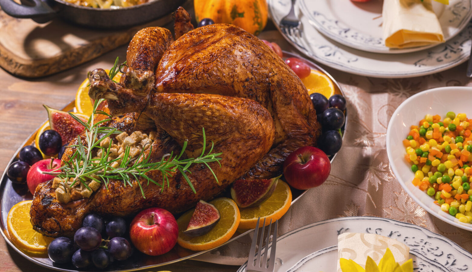A thanksgiving dinner on a table includes turkey, vegetables, and fruit.