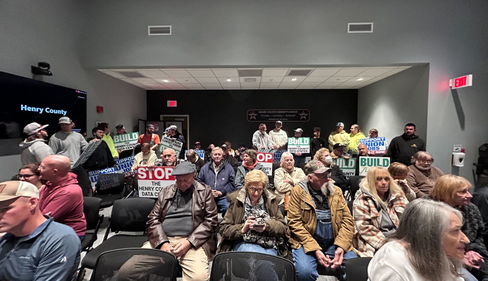 A room filled with pople looking forward. Some of them are holding signs