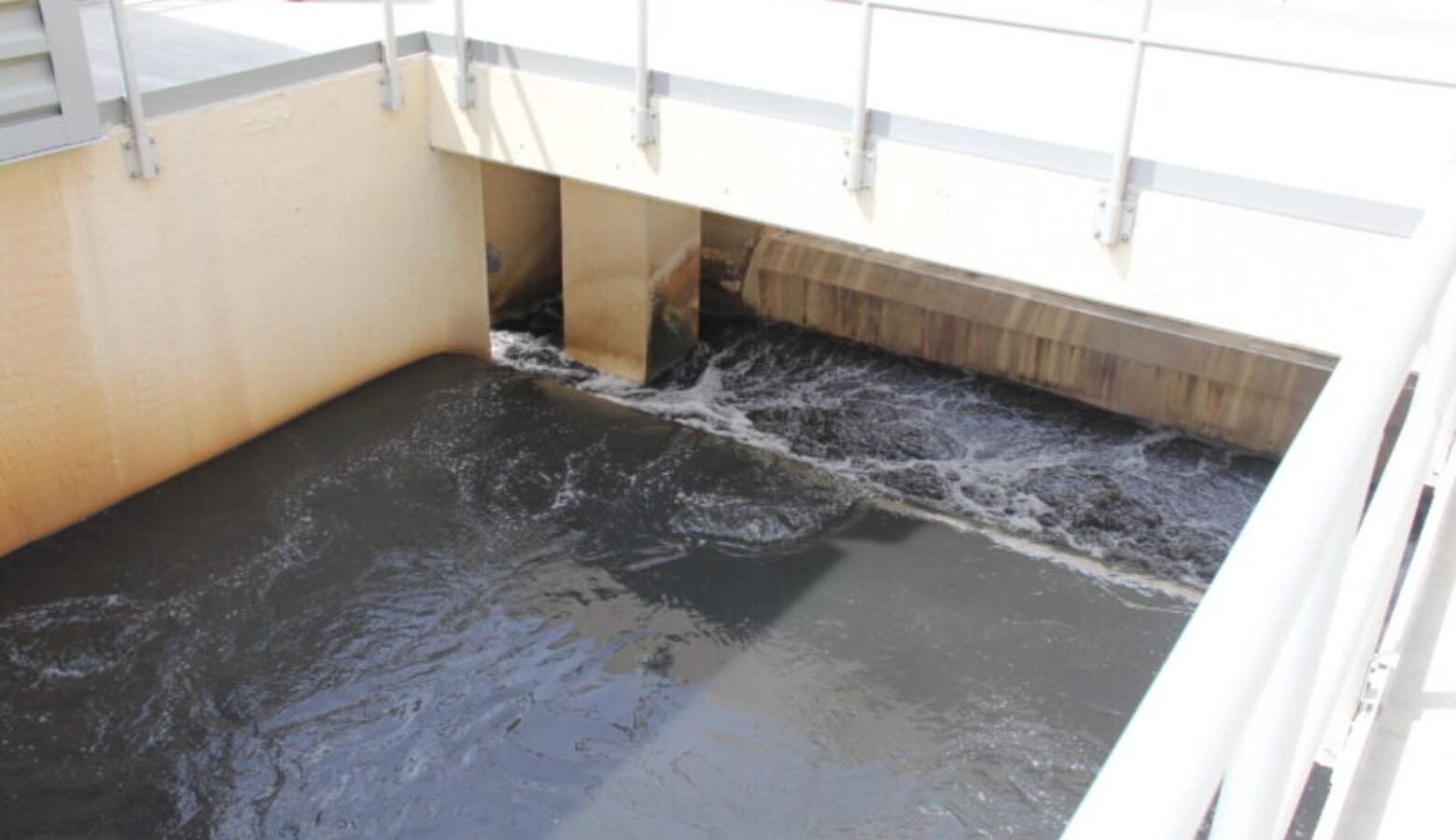 Water flows through a concrete spillway, with a white catwalk above it.