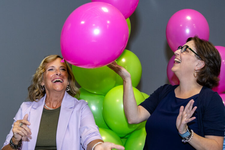 Two women are smiling and laughing as they toss balloons in the air.