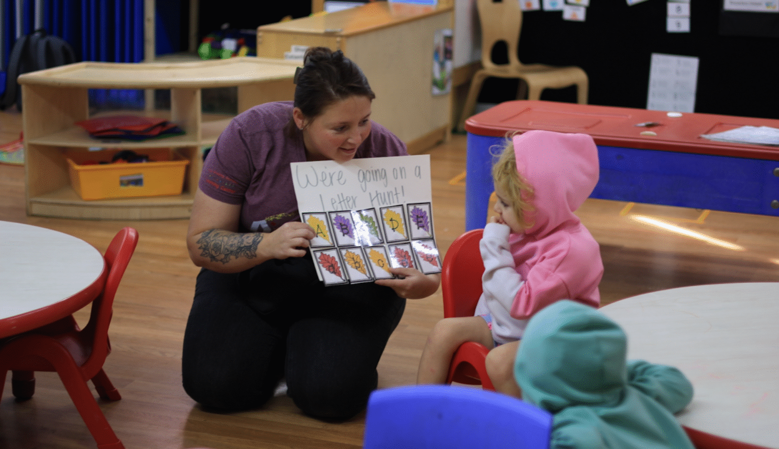 A person wearing glasses is holding a young, smiling child. In the background is another young child.