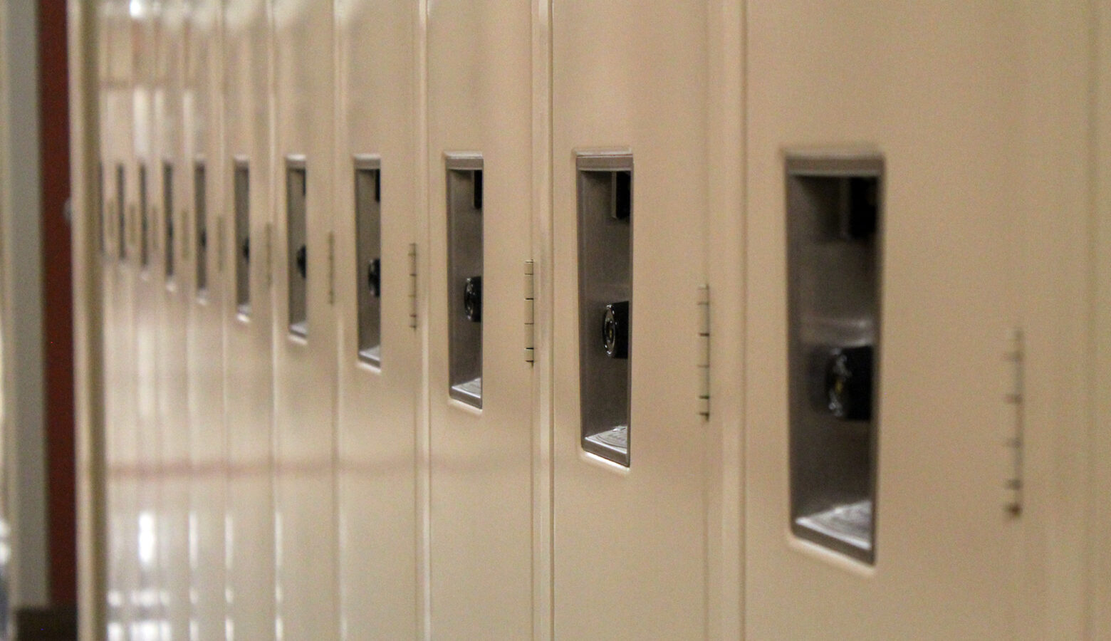 There are a line of tan lockers in a hallway.
