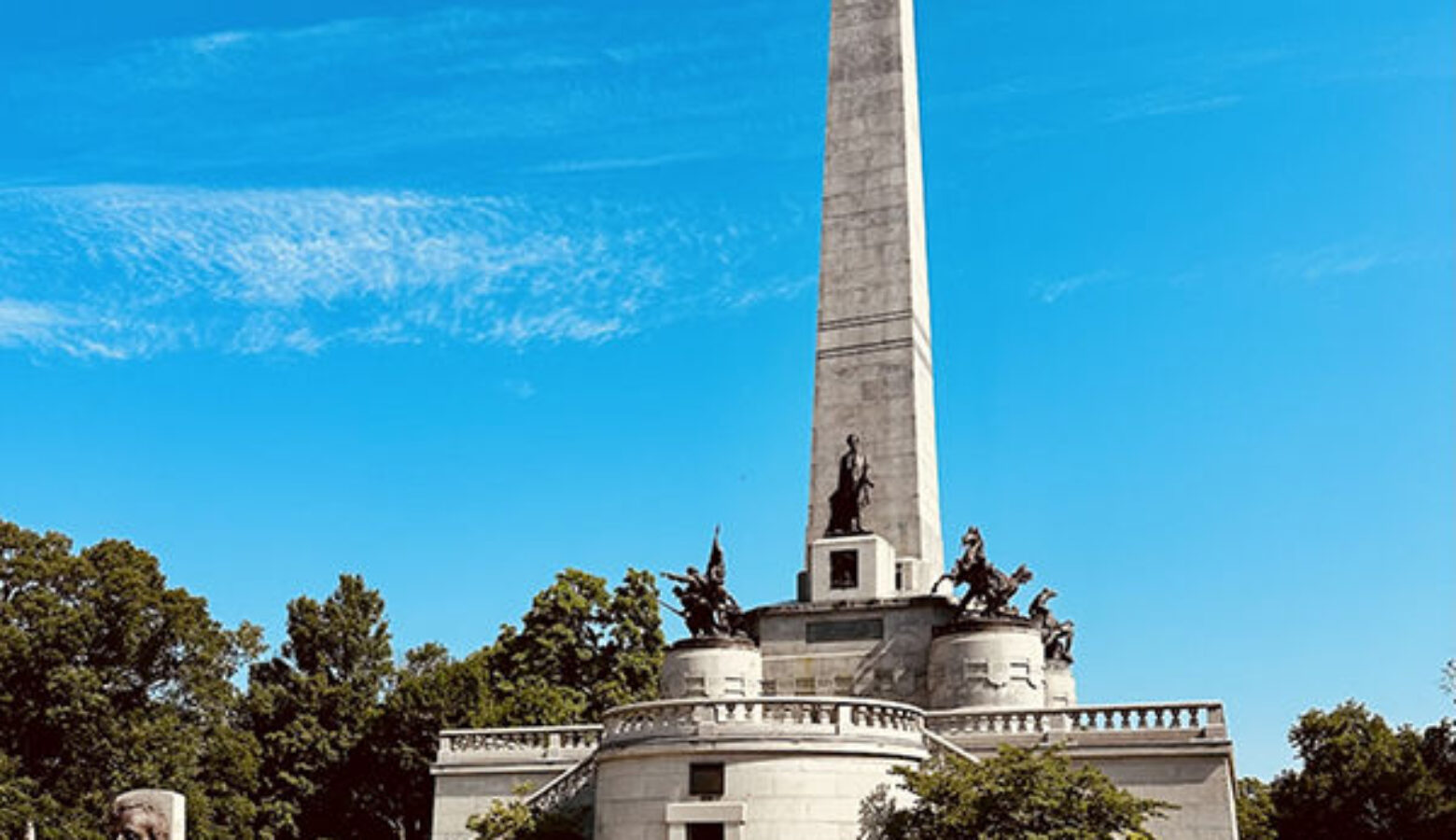 A metal statue of a man stands on a concrete platform infront of a large concrete tower.