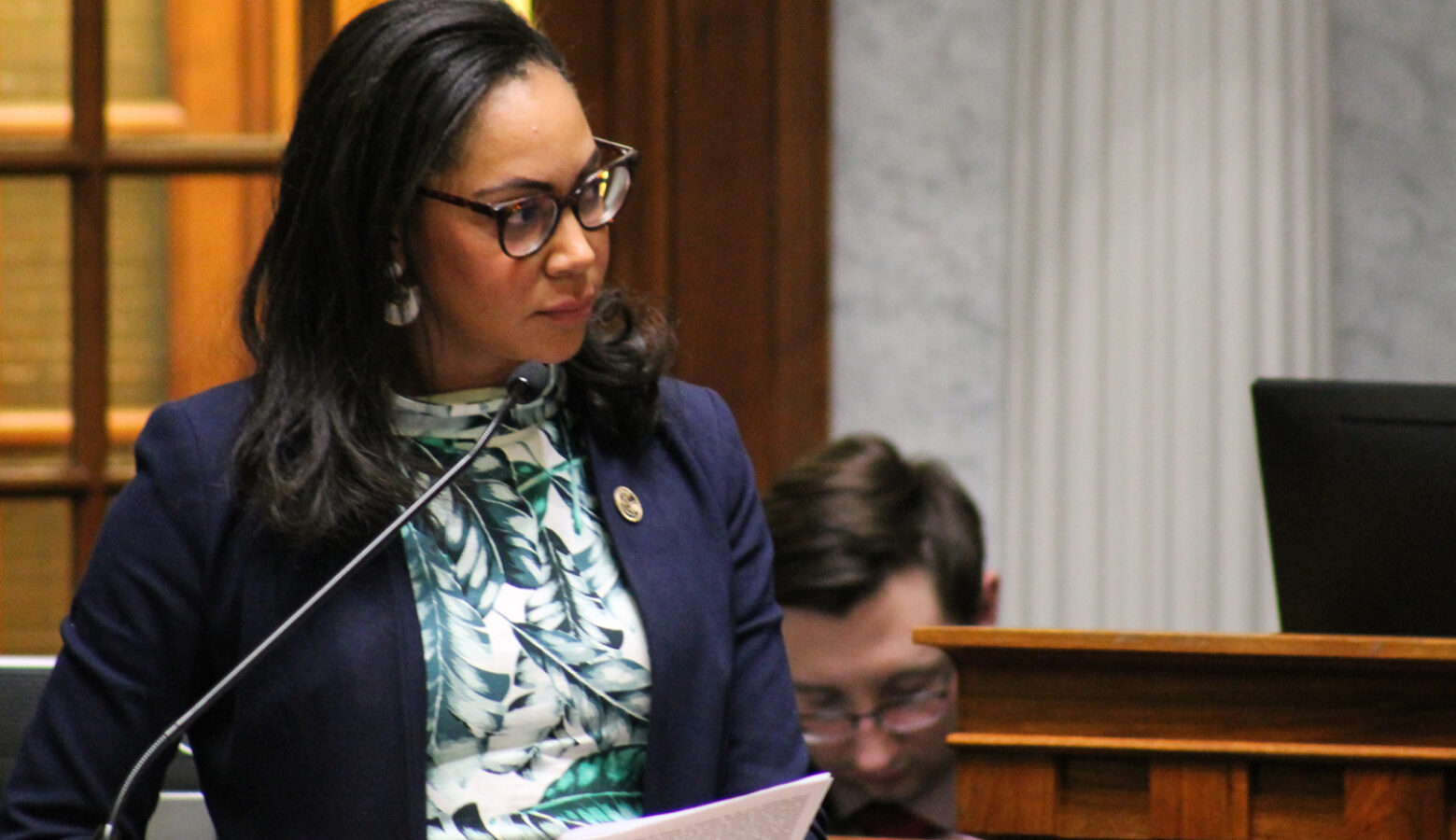 Andrea Hunley stands in the Statehouse Senate chamber, speaking into a microphone.