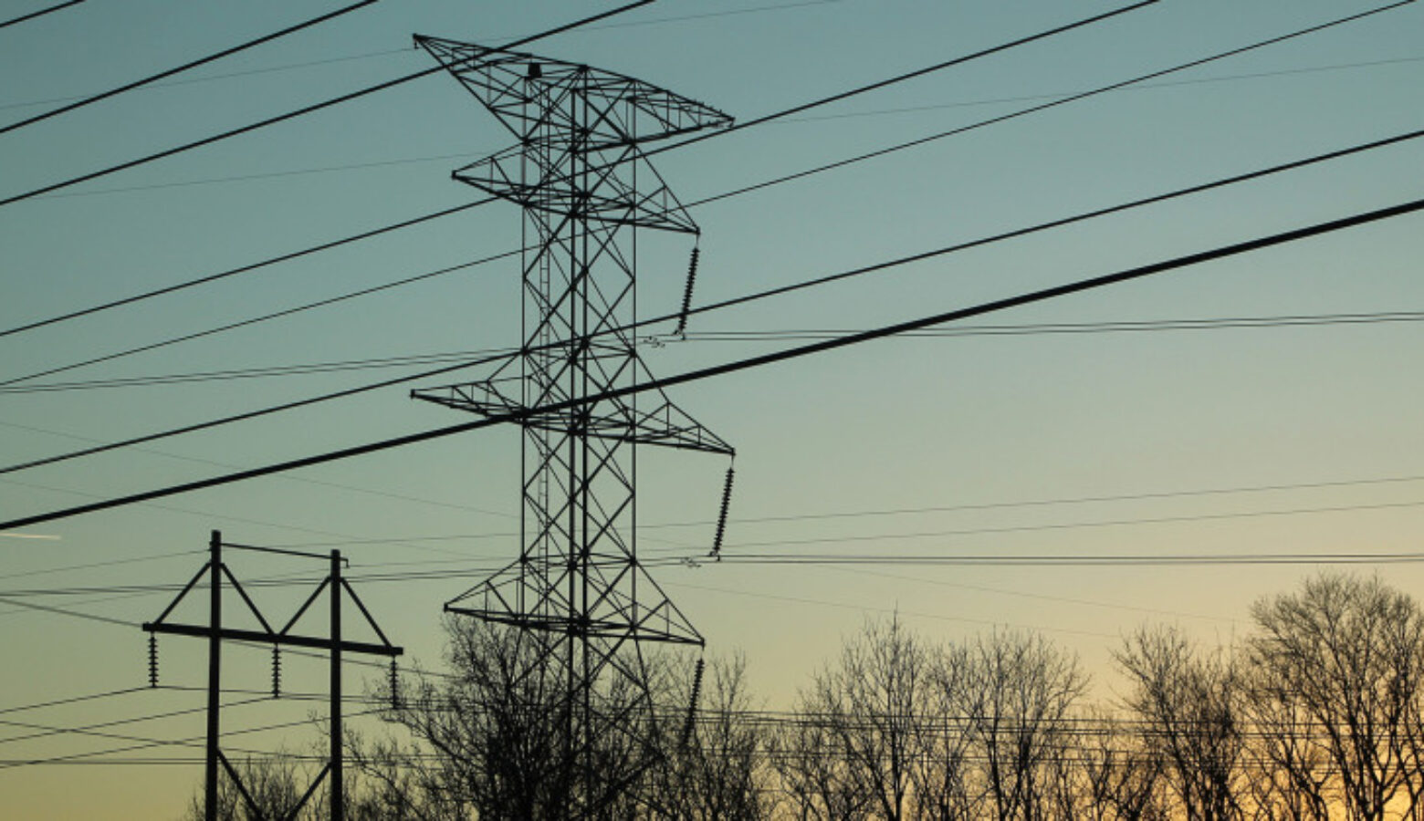 Two high voltage utility towers hold their suspended cables against a blue sky.