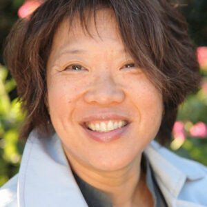 A woman with short black hair and flowers behind her smiles at the camera.