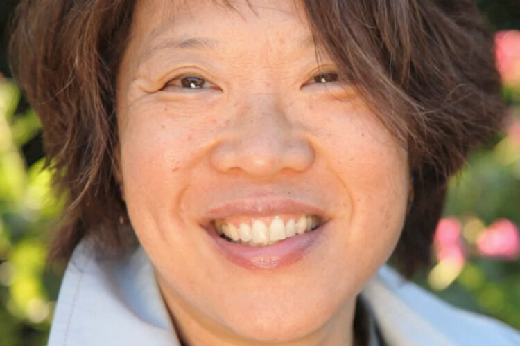 A woman with short black hair and flowers behind her smiles at the camera.