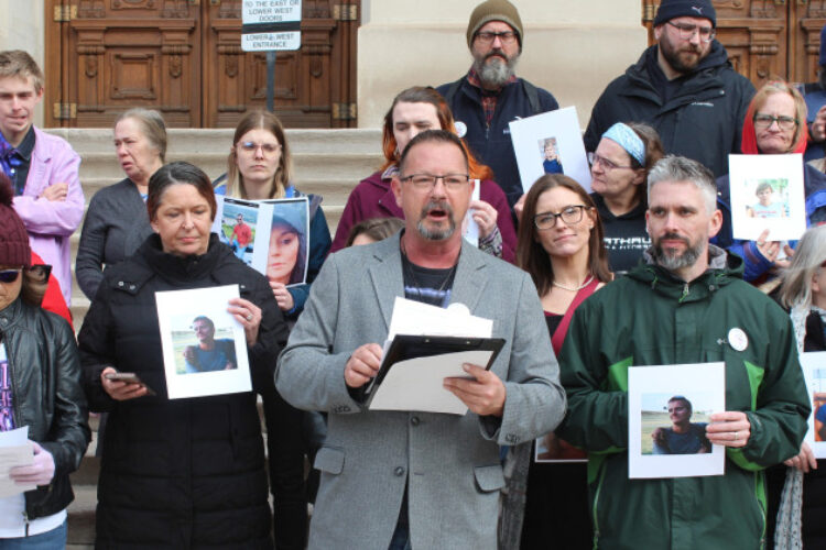 Advocates with Care, Not Cuffs gathered at the statehouse to voice opposition to bills penalizing sleeping outside and putting restrictions on needle exchange programs. Tony Hostetler (center) led members in a chant, ‘nothing about us. without us.’ The group of around two dozen protesters holds small posters at the Statehouse.
