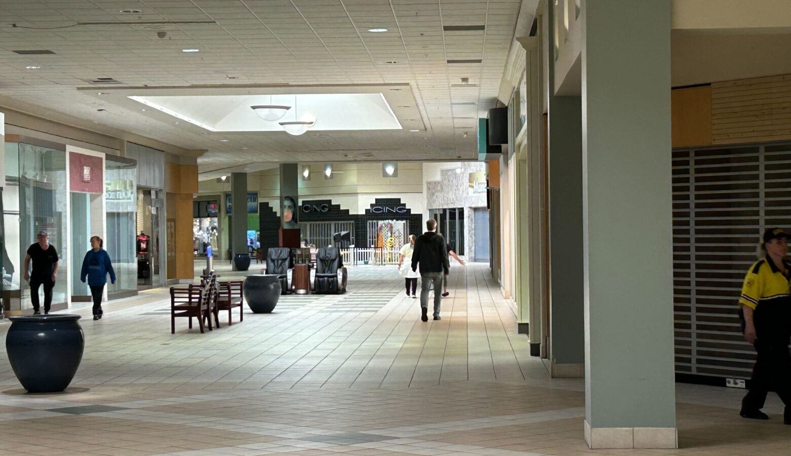 In the distance, people walk around a large hallway with some benches and potted plants, while doorways with gates surround the hallway.