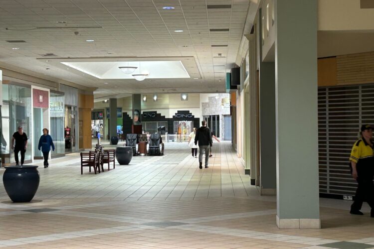 In the distance, people walk around a large hallway with some benches and potted plants, while doorways with gates surround the hallway.