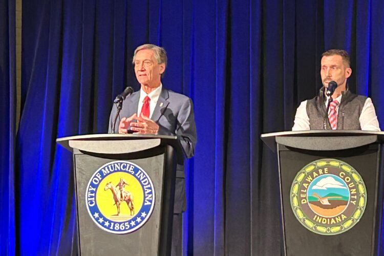 Two men stand at podiums and speak into microphones.