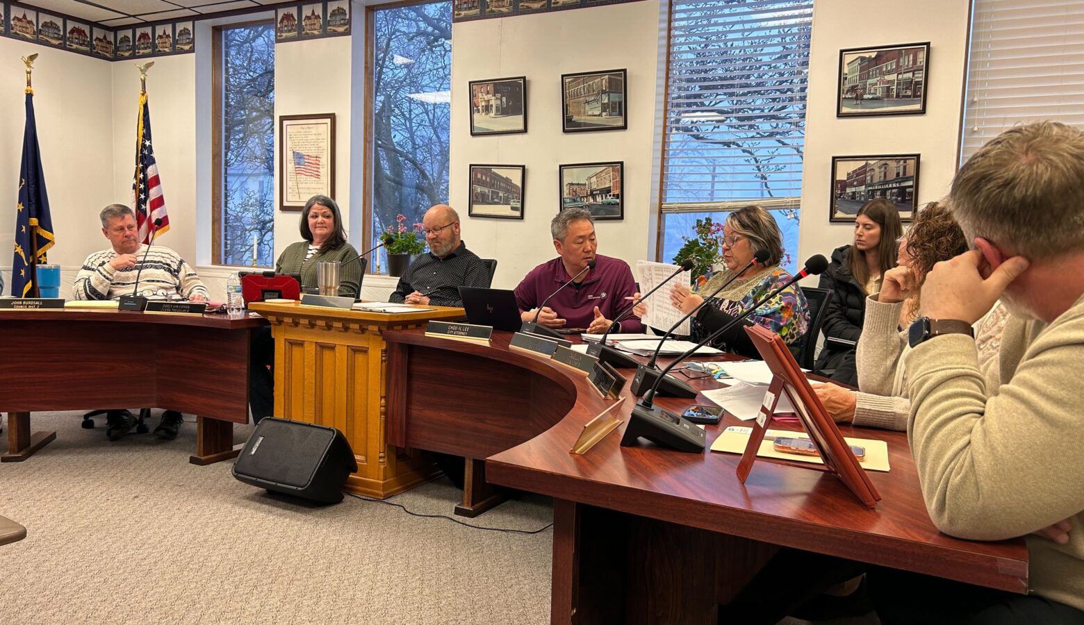 Multiple people sit at desks facing an audience sitting in chairs.