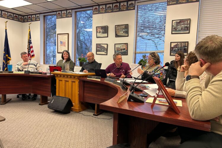 Multiple people sit at desks facing an audience sitting in chairs.