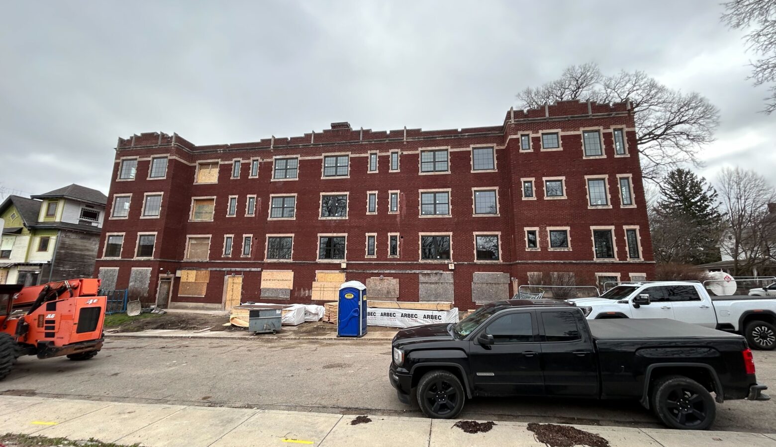 A large brick building stands on the side of a street. Plywood panels are fixed to its first floor windows.