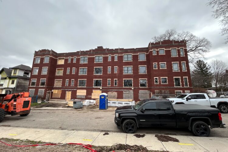A large brick building stands on the side of a street. Plywood panels are fixed to its first floor windows.