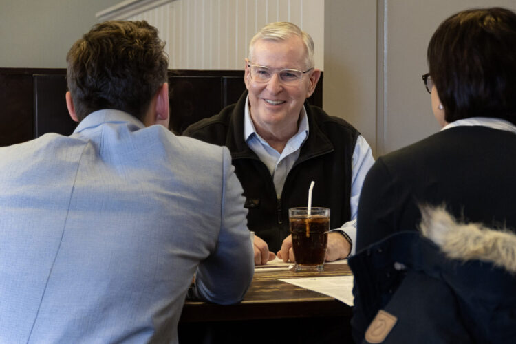 Former Indianapolis Mayor Greg Ballard smiles as he speaks with two people (whose backs are to the camera) at a restaurant.