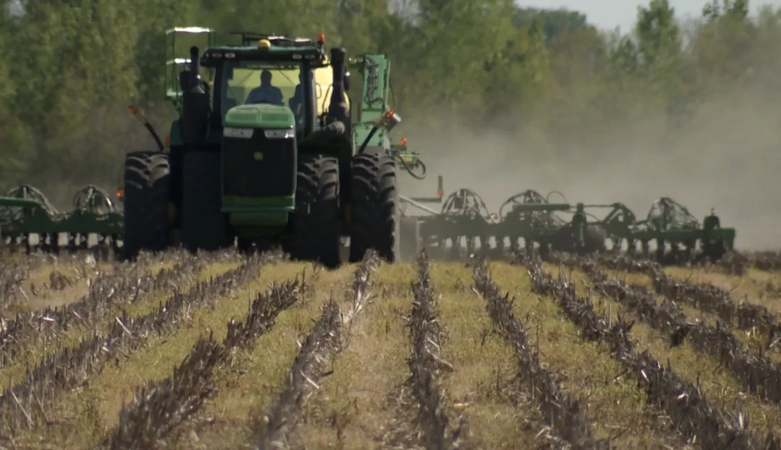 A large, John Deere planter is doing its rounds at the start of season in a tilled field.