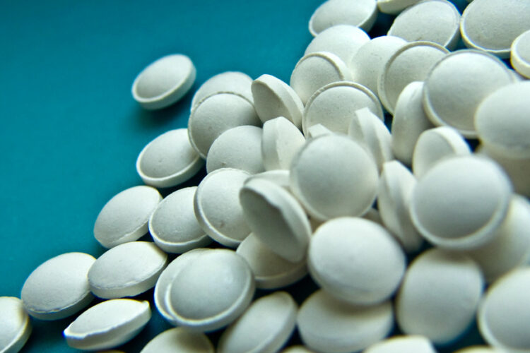 Many small white pills sit in an unorganized pile on a blue table.