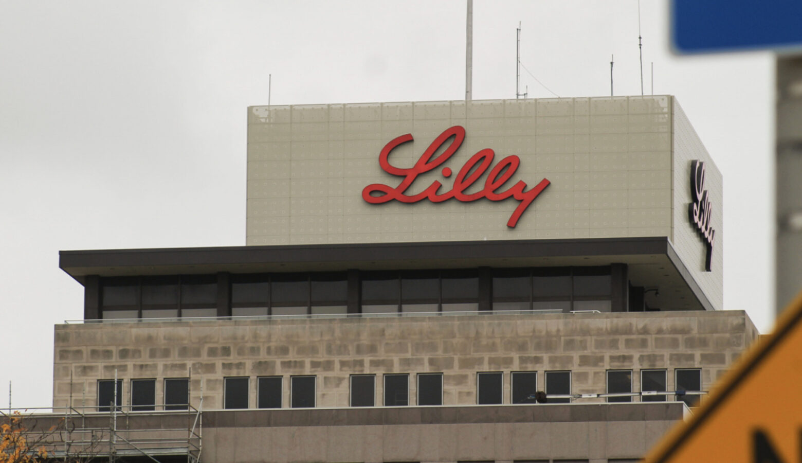 Eli Lilly's headquarters is a large building made of gray stone and glass. At its top, the word Lilly is written in red script.