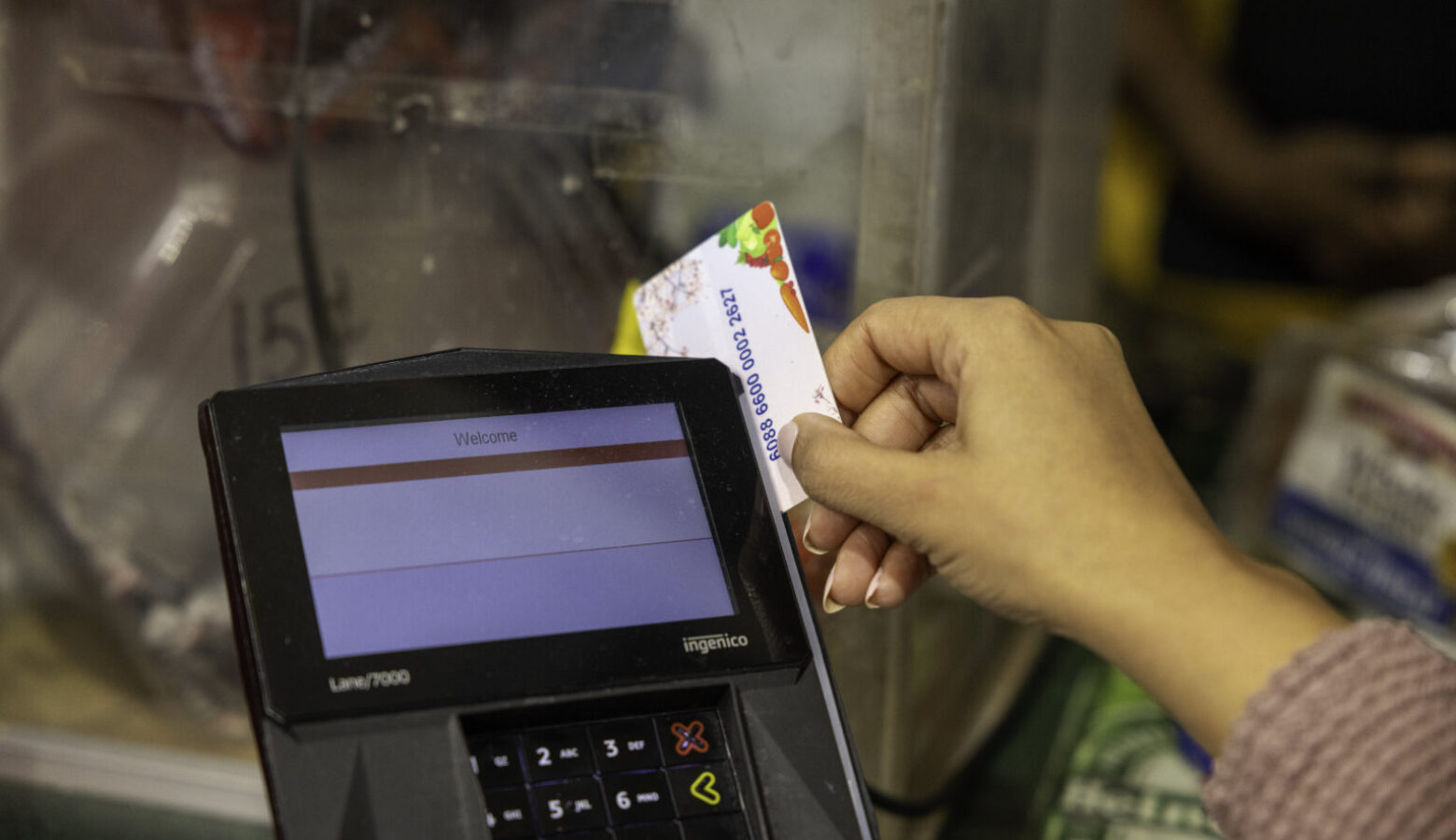 A person swipes a benefits card through a card-reader at a grocery store.