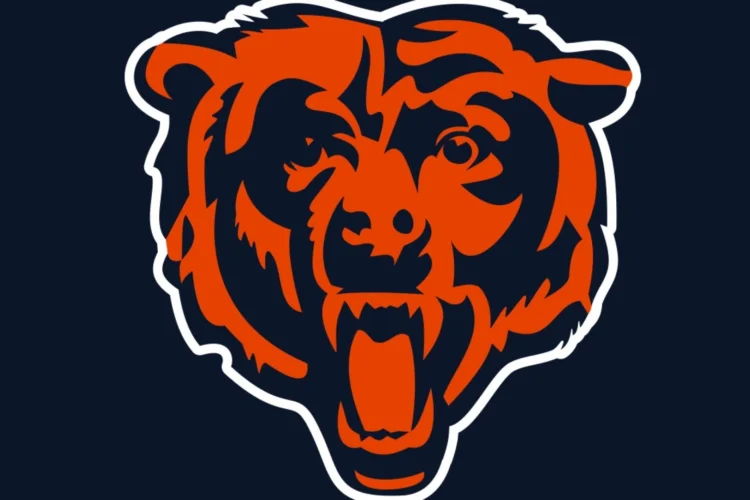 A closeup, centered image of the Chicago Bears logo with orange features and a dark blue background on the bear's face with a white outline separating the bear's head from the same dark blue in the background.
