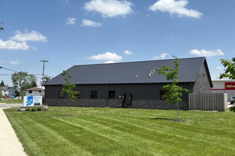 A large black building sits on a green lawn. A sign next to it reads "Muncie Crisis Center - Meridian Health Services."